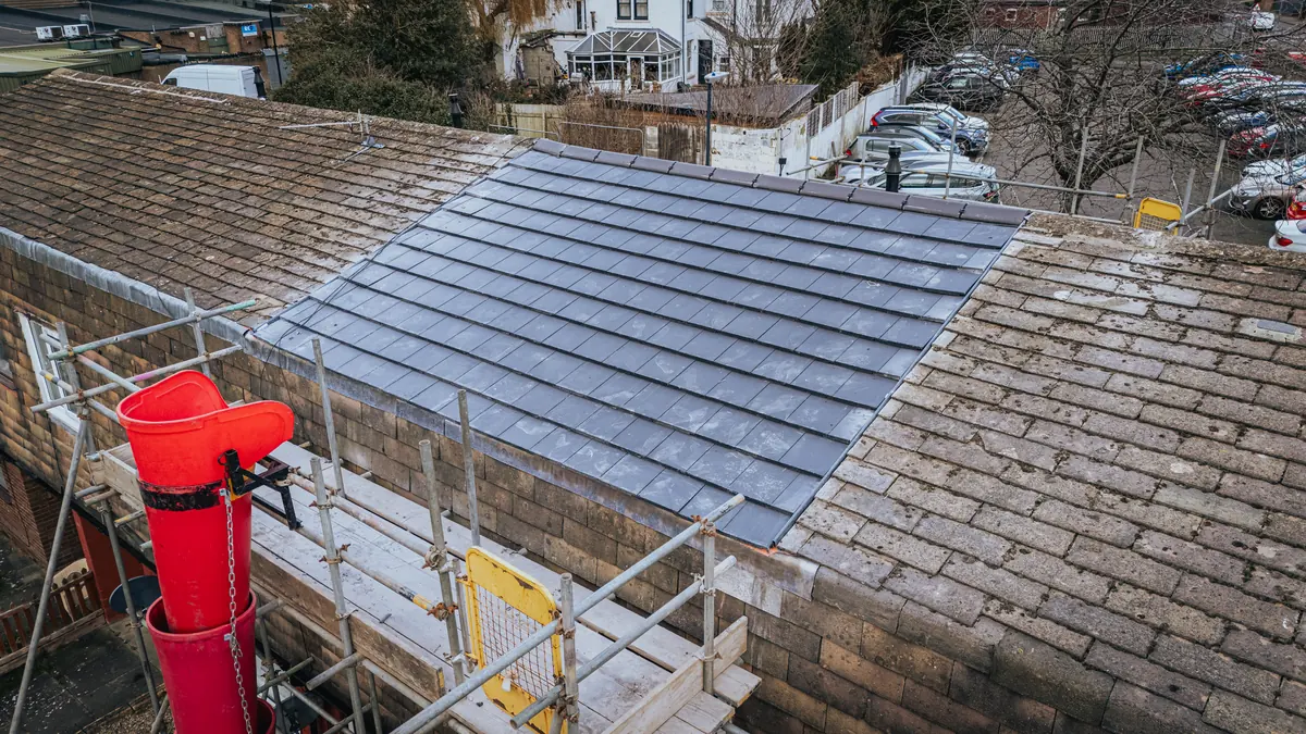Slate re-roof in progress with scaffold and debris chute, aerial view